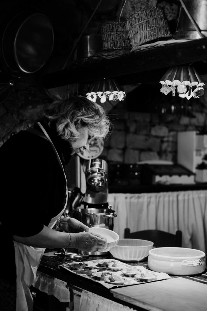 Eine Frau platziert sorgfältig Speisen auf einem Teller in einer gemütlichen, dimmigen Küche. Im Hintergrund sind Kochutensilien und eine Küchenmaschine sichtbar.