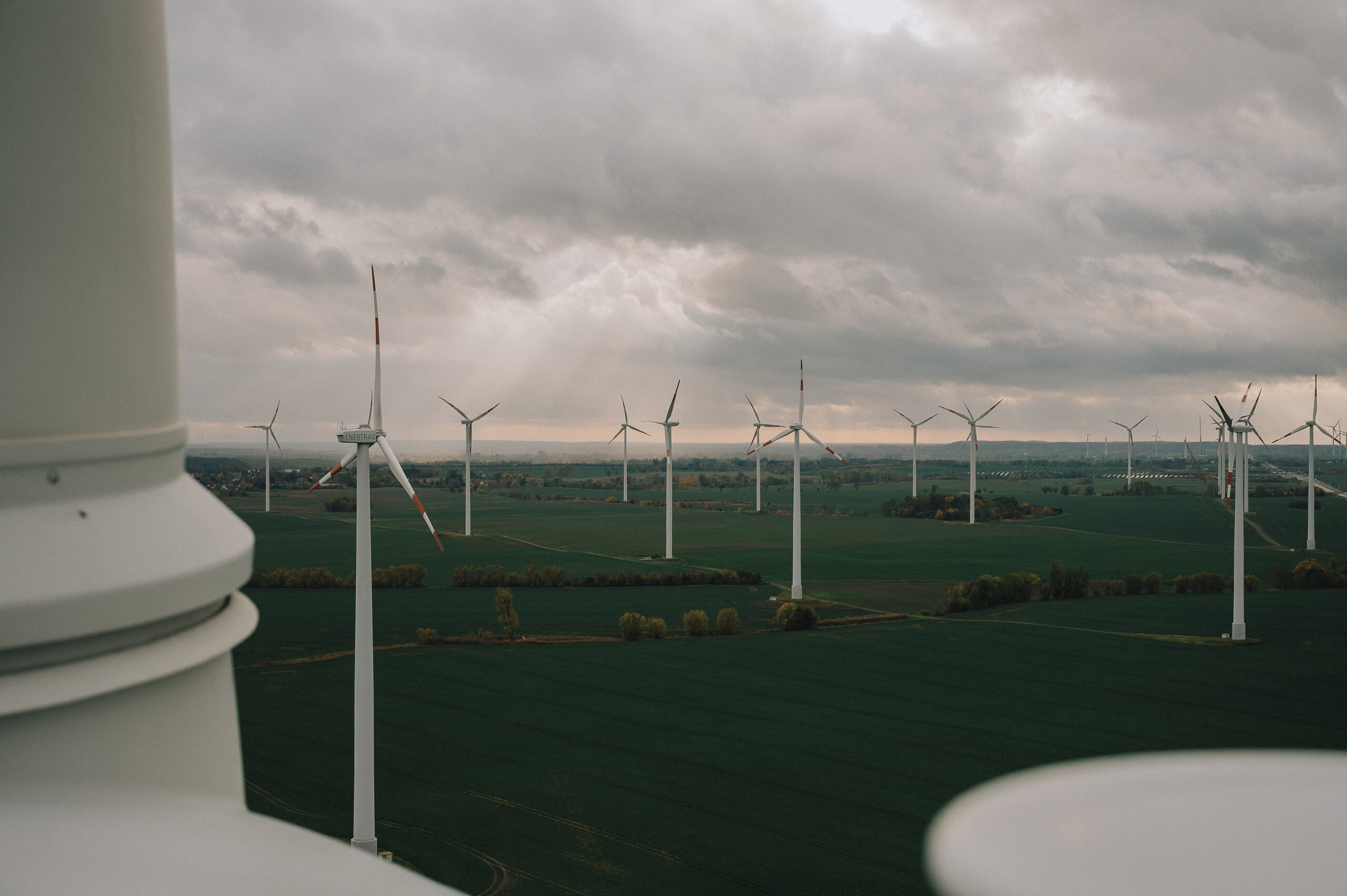 Eine Landschaft mit Windkraftanlagen, die auf grünen Feldern stehen, unter einem bewölkten Himmel. Die Windräder drehen sich sanft im Wind und symbolisieren erneuerbare Energie, passend zu Enertrag und Employer Branding.