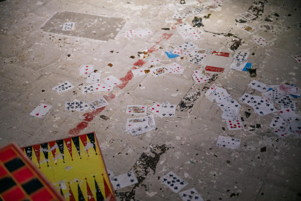 Eine unordentliche Fläche mit verstreuten Spielkarten auf einem schmutzigen Boden. Einige Karten sind sichtbar, während ein Teil eines Brettspiels in der linken unteren Ecke zu sehen ist. #Dye-2-greenland