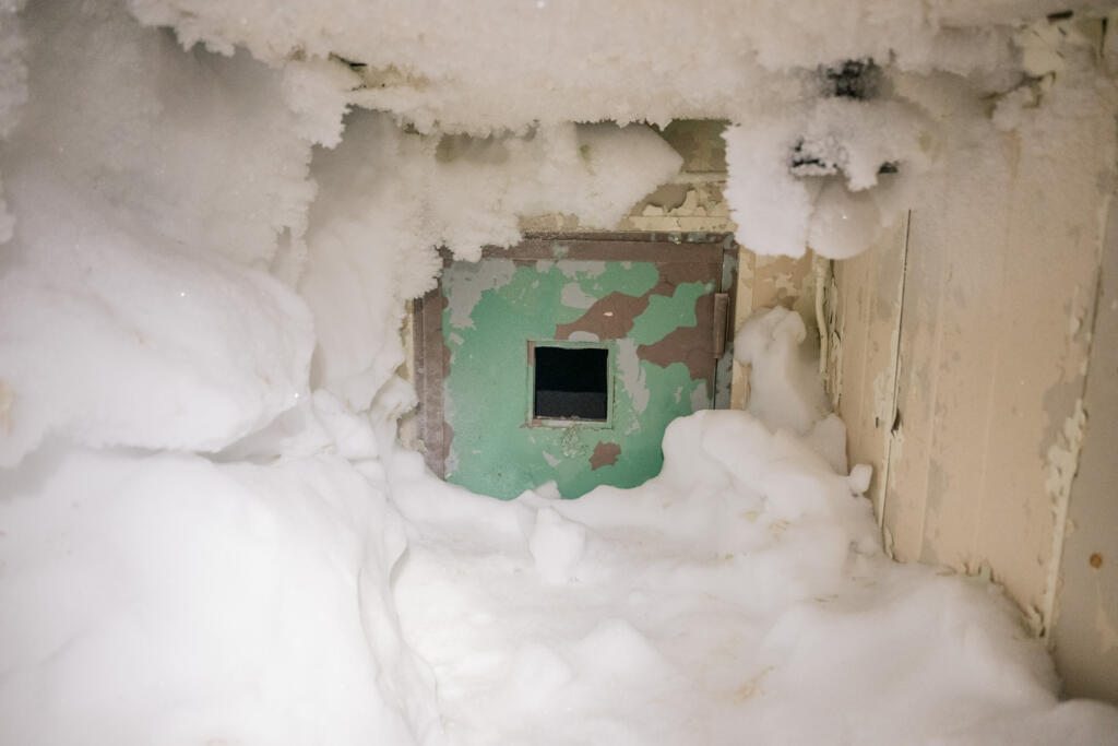Ein schneebedeckter Eingang zu einem kleinen Raum mit einer grünen Wand. Die Umgebung ist von Schnee und Eis umgeben, wodurch der Eindruck eines verlassenen oder ungenutzten Bereichs entsteht. #Dye-2-greenland