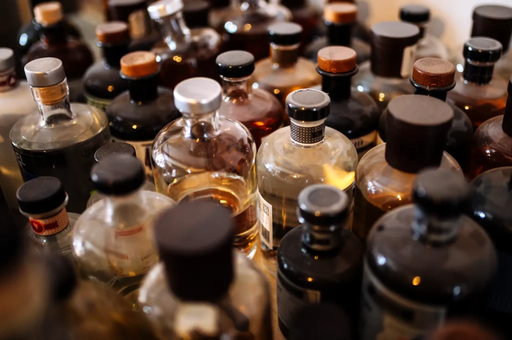 Eine Anordnung von verschiedenen Flaschen mit alkoholischen Getränken in verschiedenen Größen und Farben, sichtbar auf einem Tisch. Einige Flaschen haben Korken, während andere Schraubverschlüsse besitzen.