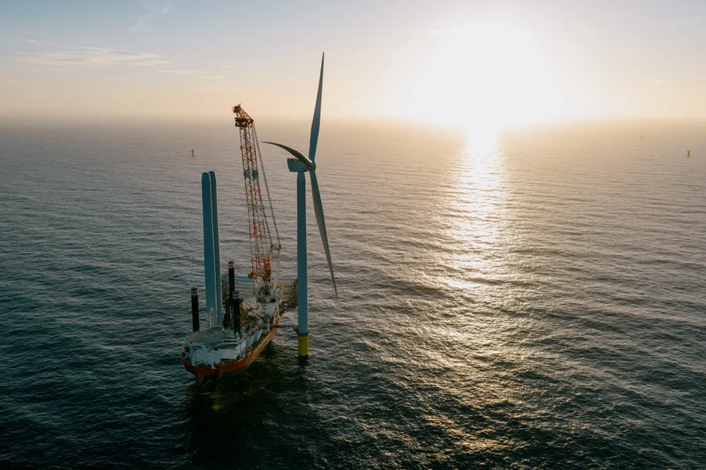 Die erste fertige Windturbine des Offshore Windpark THOR im Sonnenaufgang. Daneben steht das Jackup Vessel Offshore Schiff Brave Tern.